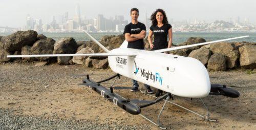 The co-owners of the MightyFly company stand behind the MightyFly MF-100, a white hybrid-electric vertical takeoff and landing aircraft that will be used for air cargo.