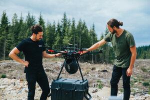 Two men hold a drone used to plant trees via the air.