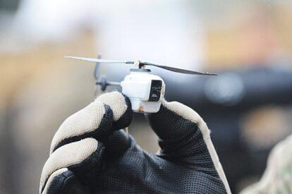 A gloved hand holding a white miniature drone.