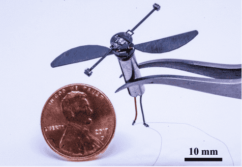 Tiny flying bot suspended by tweezers next to penny.