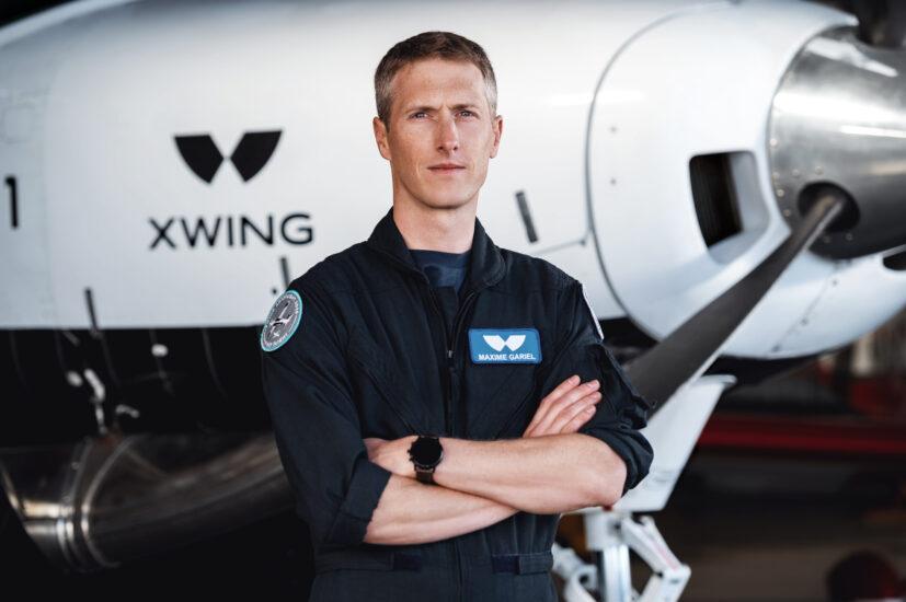 A man standing with arms crossed in front of an XWing aircraft.