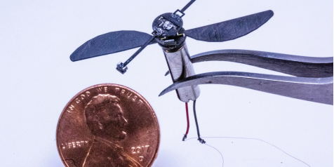 Tiny flying bot suspended by tweezers next to penny.